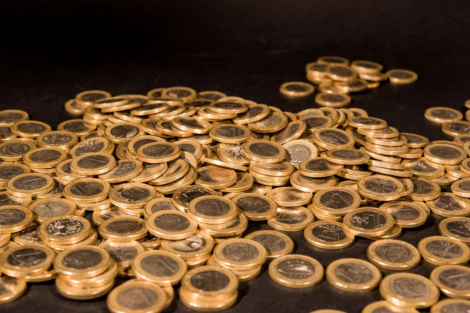 Moedas de um euro espalhadas sobre uma superfície escura.