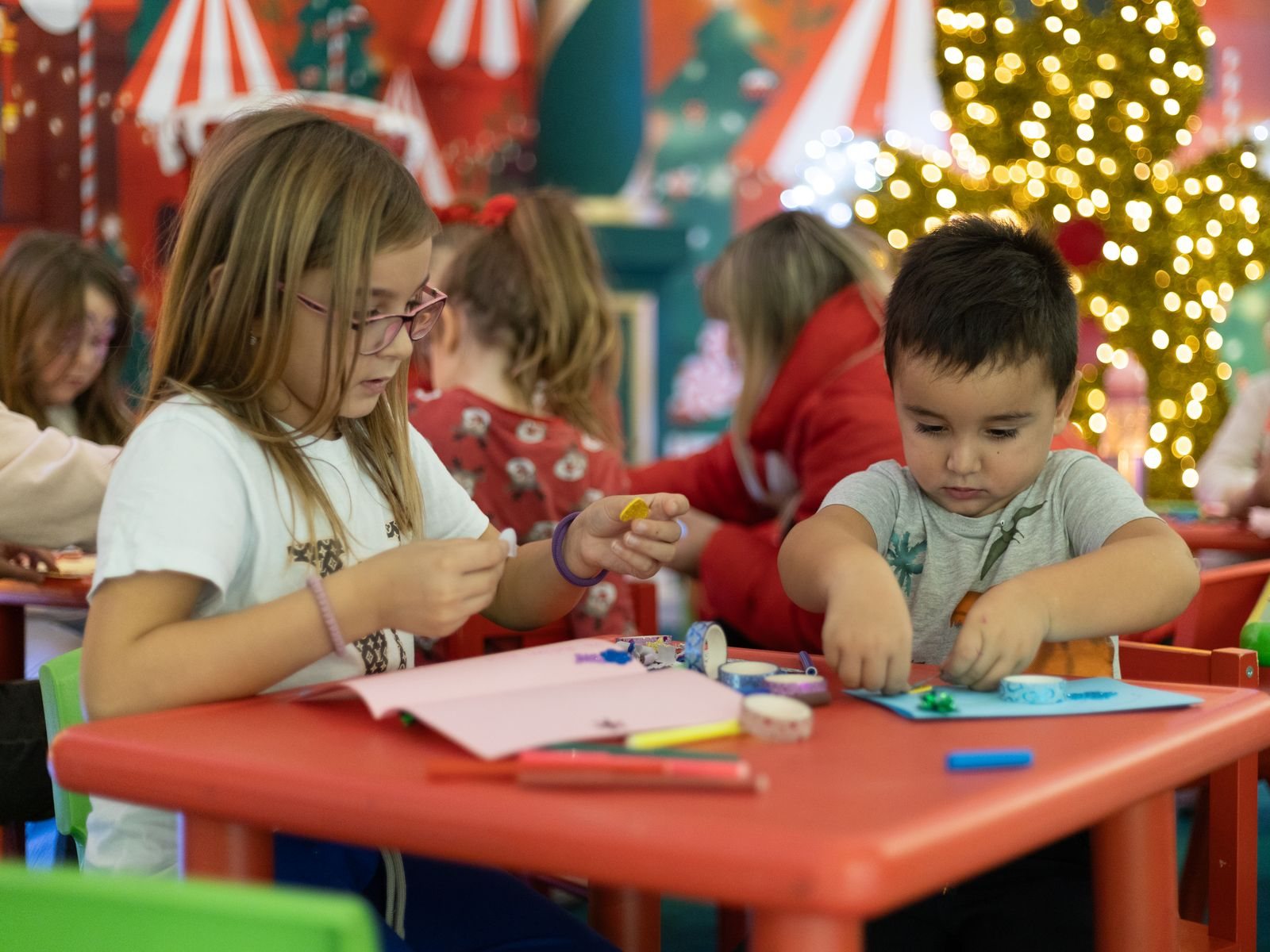 Crianças a preparar trabalhos manuais numa sala decorada para o Natal.